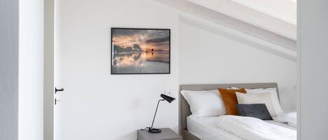 Een slaapkamer met een bed, nachtkastje, lamp en een lijst met een afbeelding aan de muur.