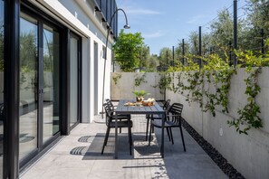 Eine Terrasse mit Tisch und Stühlen, eine Betonwand mit Kletterpflanzen und ein Glastür-Eingang.