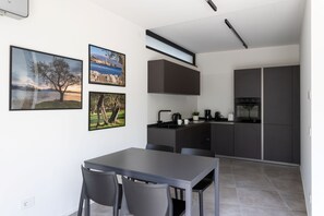 A modern kitchen with dark cabinetry, a dining area with a table and chairs, and three framed landscape photographs on the wall. - Casa Franzosi - Leccino Luxury (Puegnago sul Garda)