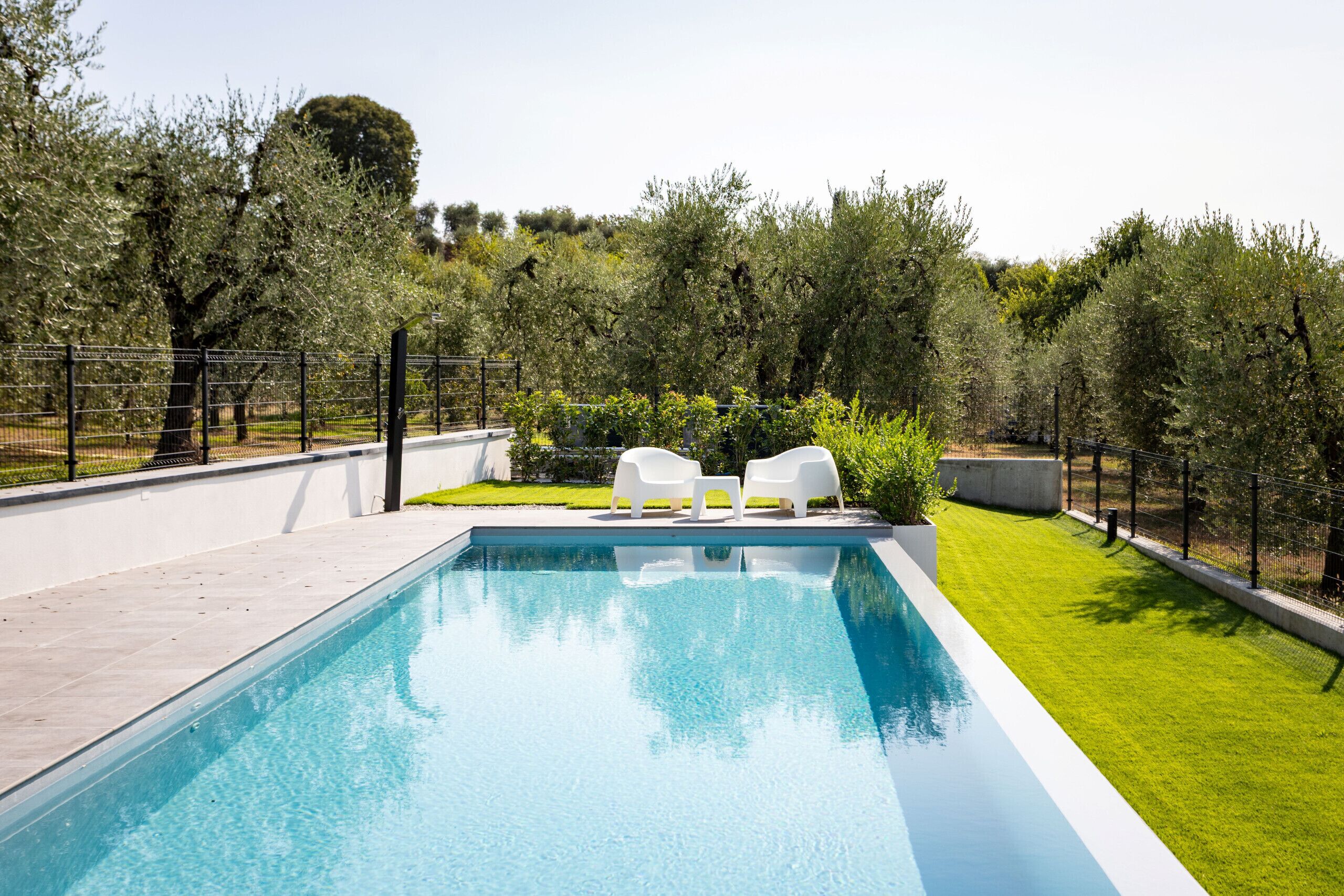 Une piscine à l’eau d’un bleu cristallin, entourée d’une barrière basse, et deux chaises longues blanches placées face à la piscine.