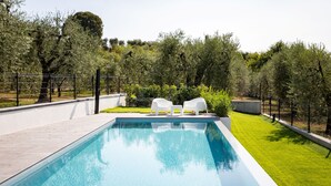 A swimming pool with a clear blue water surface, surrounded by a low fence, and two white lounge chairs facing the pool.