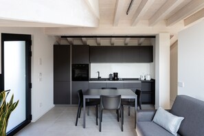 A modern kitchen with dark cabinetry, a central island, and a dining area with chairs. - Casa Valtenesi - 3 Sensi (Puegnago sul Garda)