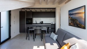 Una cucina moderna con mobili scuri, una zona pranzo con divano e poltrone grigi e un'ampia finestra.