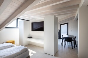 A modern bedroom with a sloped ceiling, a bed, a bench, and a TV mounted on the wall. - Casa Valtenesi - 3 Sensi (Puegnago sul Garda)