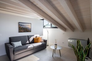 A modern living room with a grey sofa, a small round table, and a large window. - Casa Valtenesi - 3 Sensi (Puegnago sul Garda)