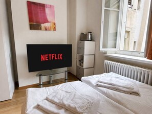 Ein Hotelzimmer mit einem Bett, einem Fernseher, der 'NETFLIX' anzeigt, einem Heizkörper und einem Fenster.
