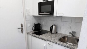 A compact kitchen with white cabinets, a built-in microwave, a kettle, and a stainless steel sink. - Cozy Studio in the Heart of Zurich - Stork 25 (Zürich)