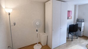 A room with a standing fan, a desk with a chair, and a wardrobe. - Cozy Studio in the Heart of Zurich - Stork 25 (Zürich)