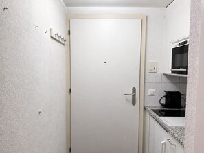 A small, white-walled kitchen with a microwave, a coffee maker, and a door with a handle. - Cozy Studio in the Heart of Zurich - Stork 25 (Zürich)