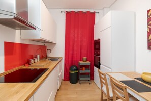 A compact kitchen with a red curtain, a sink, a stove, and a small dining area with chairs and a table. - Quasi per casa By Dimorra (Naples)