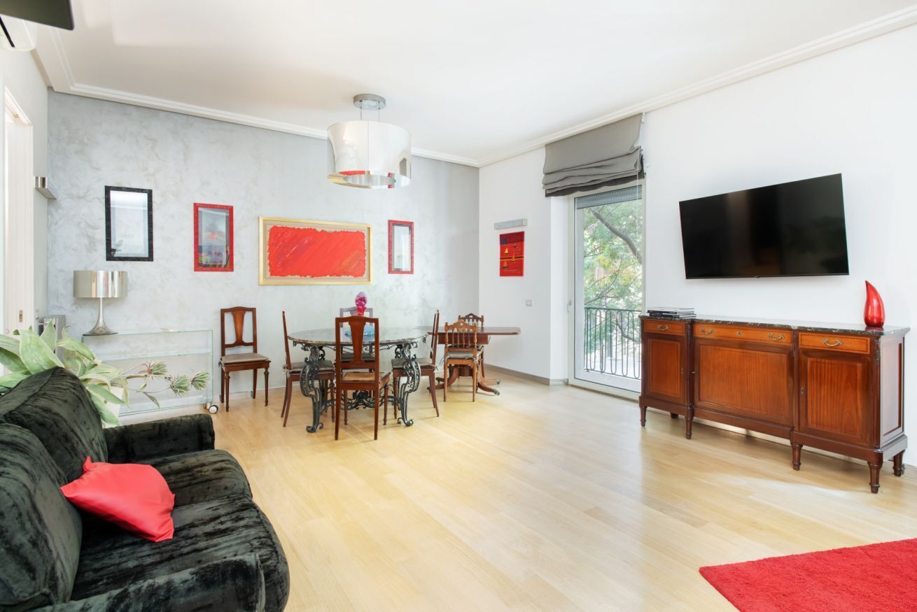 Sala de estar con sofá negro, mesa de comedor, sillas, televisor y alfombra roja.