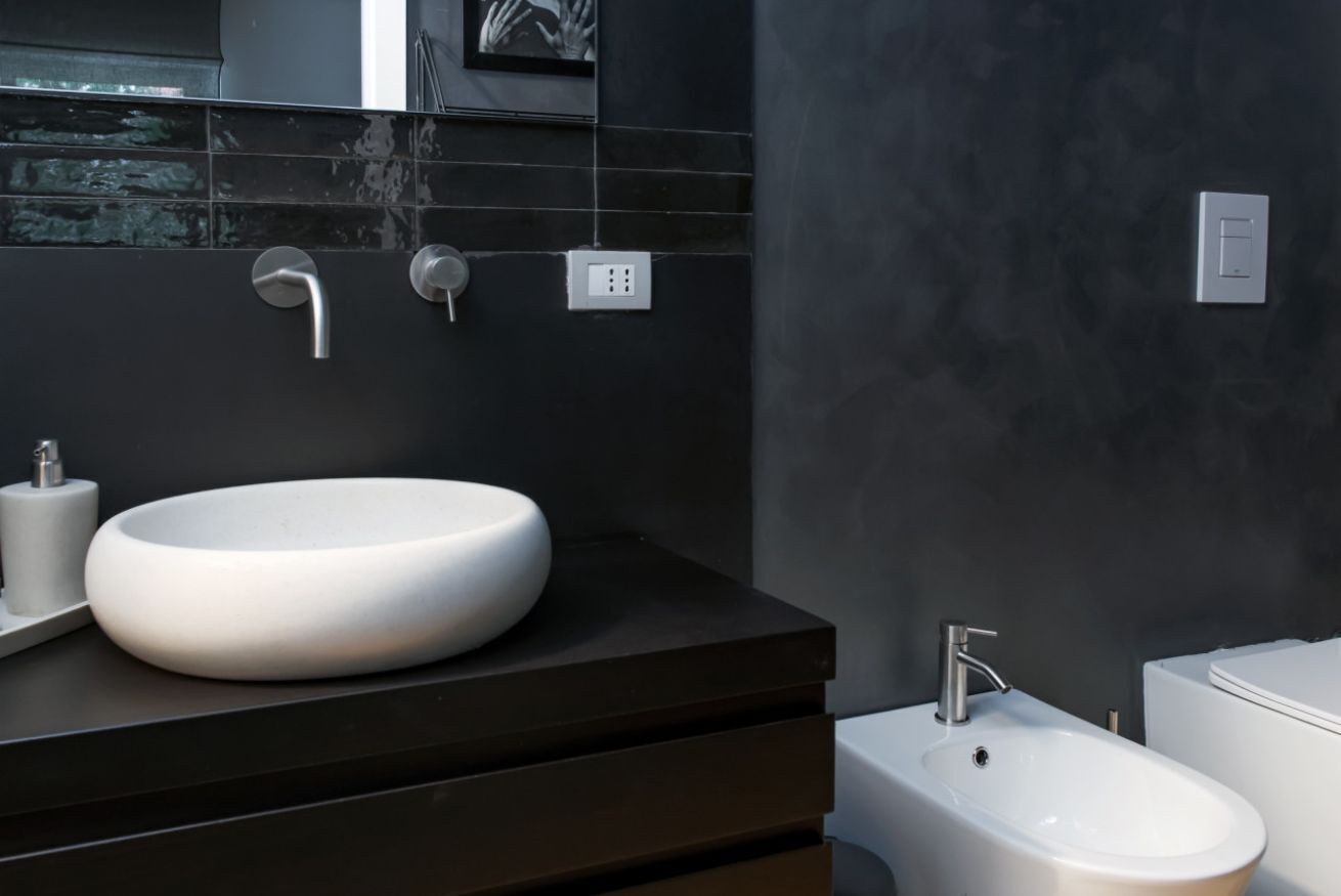 A modern bathroom with a round white sink, a dark countertop, and a bidet.
