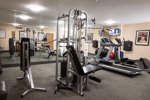 A gym with various exercise equipment, including a treadmill, weight machines, and a mirrored wall.