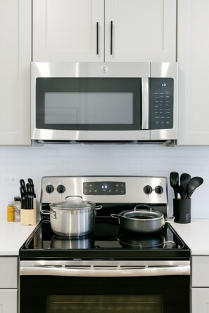 A kitchen with a stainless steel microwave and stove, white cabinets, and a tiled backsplash. - Stunning 1BR Getaway I Washer-Dryer-Pool (Sherman)