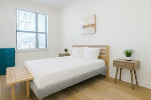 Une chambre à coucher comprenant un lit, un bureau, une chaise, une table de chevet avec une plante et une fenêtre avec des stores.