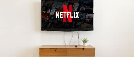 A television mounted on a wall with a Netflix logo, a wooden cabinet below, and a small plant on top of the cabinet.