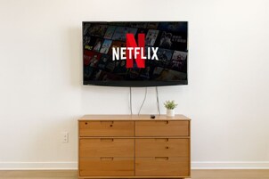 Un televisor montado en la pared con el logotipo de Netflix, un mueble de madera debajo y una planta pequeña encima del mueble.