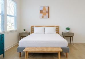 Un dormitorio ordenado con cama, mesitas de noche, un banco y una obra de arte en la pared.