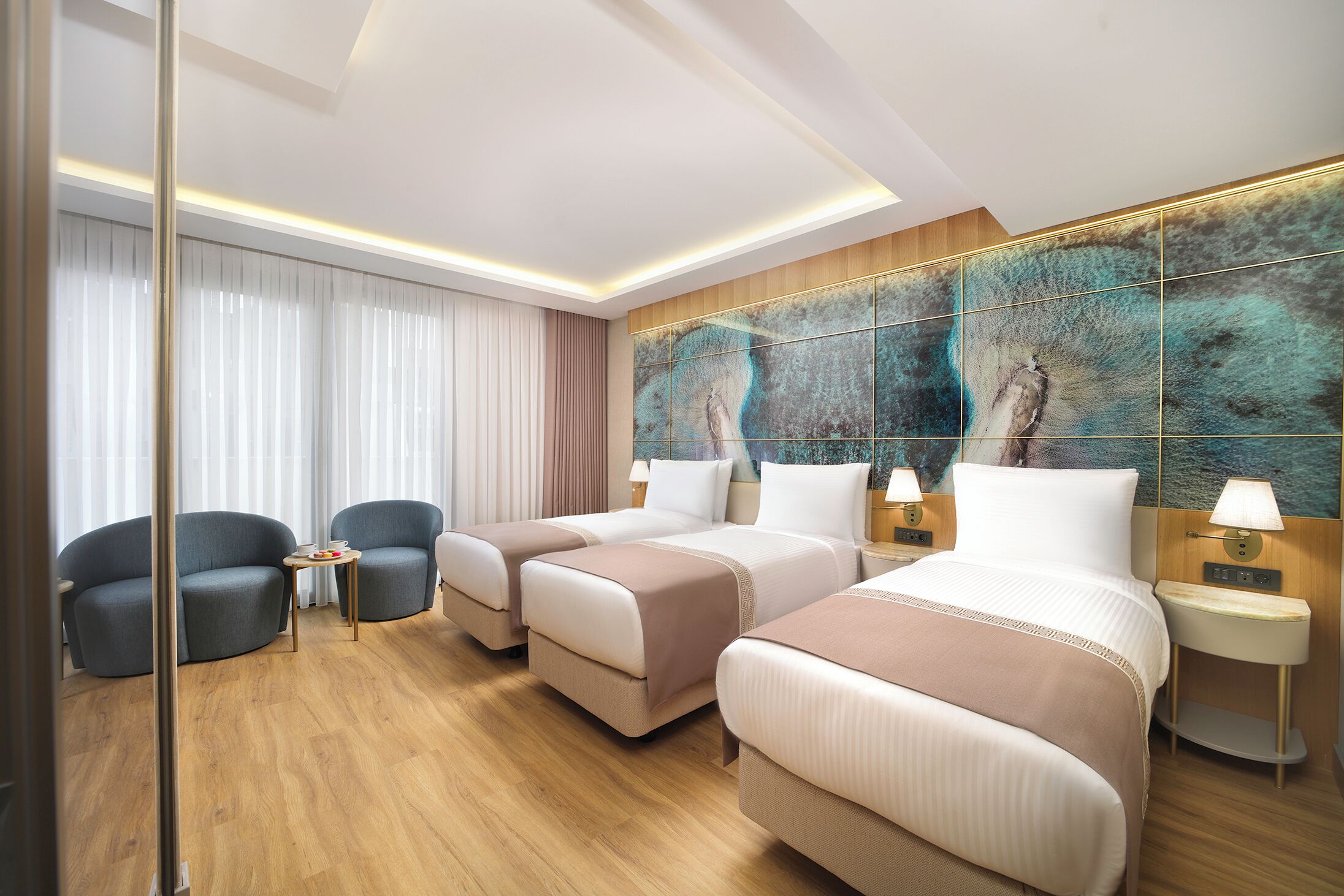 A hotel room with two beds, a sitting area with chairs, a large mirror, and a wall with a textured artwork.
