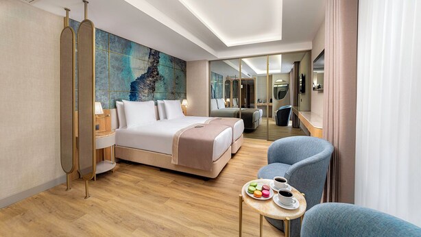 Una habitación de hotel moderna con una cama grande, una zona de estar con una pequeña mesa y un espejo amplio.