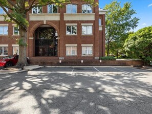 En byggnad i flera våningar, byggd av tegel, med en huvudentré, parkeringsplatser och ett träd i förgrunden.