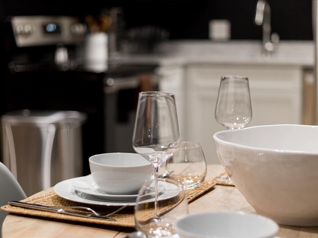 Una mesa de comedor con un bol blanco, una copa de vino y un vaso transparente.