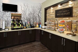 A breakfast station with a sign offering free daily breakfast, a coffee station, and various food items.