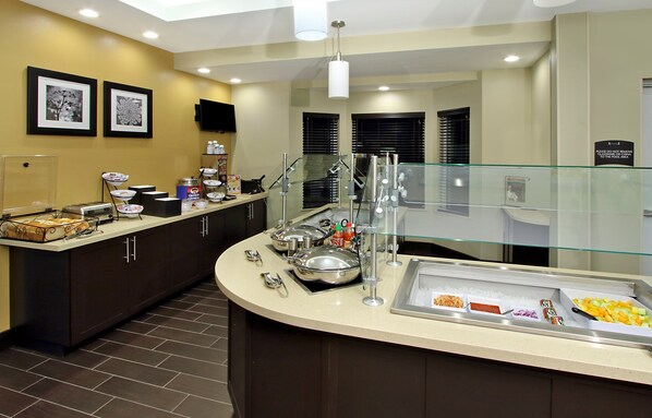 Un espace pour le petit-déjeuner dans un hôtel, avec un buffet, une rambarde en verre et un escalier.
