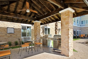 An outdoor patio with stone pillars, a grill, and seating. - Accessible 2BR Suite | Free Daily Breakfast + Pool (Houston)
