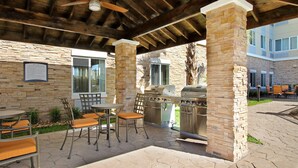 Une terrasse extérieure avec des piliers en pierre, un barbecue et des sièges.