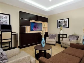 A modern living room with a flat-screen TV, sofas, a coffee table, and a bookshelf. - Accessible Queen Studio w/ Free Breakfast + Pool (Houston)