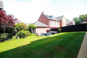 Ein Wohngebiet mit gepflegtem Rasen, einer Terrasse mit Gartenmöbeln und einem Ziegelhaus mit Satteldach.