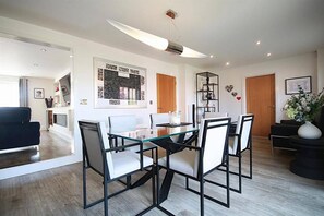 Un comedor moderno con una mesa de vidrio y sillas de metal, una lámpara colgante y una estantería.