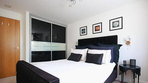 Un dormitorio con una cama grande, un armario, una mesita de noche y una lámpara de pared.