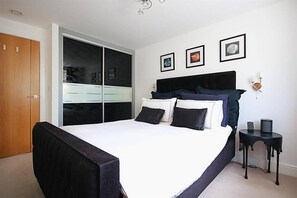 Un dormitorio con una cama grande, un armario, una mesita de noche y una lámpara de pared.