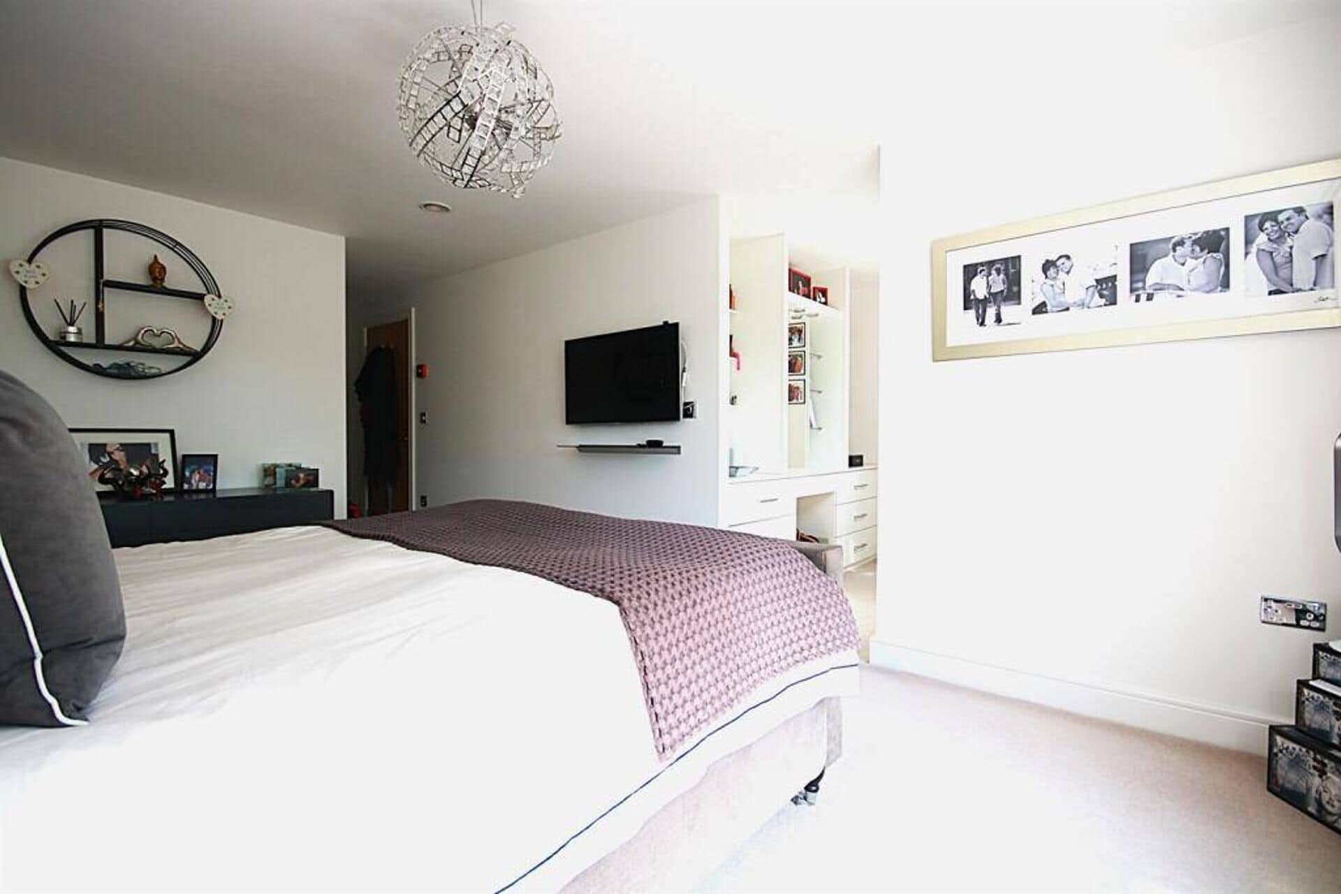 Een slaapkamer met een bed, een televisie, een dressoir en een wand met ingelijste foto's.