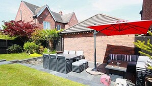 Un patio trasero con zona de estar, mobiliario exterior y un paraguas rojo.