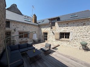 A stone building with a wooden deck, outdoor seating, and a chimney. - Stone house with a hot tub - 4 bedrooms - 800 m from the beach - Batz-sur-Mer (Batz-sur-Mer)