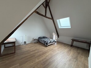 Una habitació amb sostre inclinat, un llit amb roba de llit estampada, una taula de nit i una taula petita amb una làmpada.