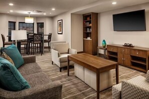 A living room with a sofa, armchair, wooden coffee table, TV, bookshelf, and a dining area with chairs and a table.