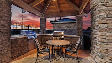 An outdoor patio with a stone wall, a round table, and metal chairs.
