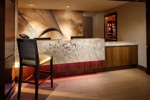 A reception desk with a marble top, a wooden chair, and a wall with a geometric design.