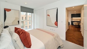 Quarto de hotel moderno com uma cama grande, duas pinturas abstratas, uma janela com vista para edifícios e um espaço de jantar separado.