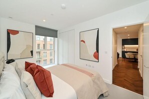 Ein modernes Hotelzimmer mit einem großen Bett, zwei abstrakten Gemälden, einem Fenster mit Blick auf Gebäude und einem separaten Essbereich.