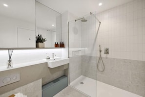 Ein modernes Badezimmer mit einer gläsernen Dusche, einem weißen Waschbecken und einem Spiegel über dem Waschtisch.