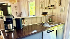Una cocina con cafetera, lavamanos y ventana.