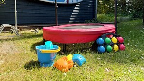 Un trampolín, una tabla de surf y pelotas de colores en un jardín cubierto de césped.