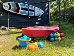 A trampoline, a surfboard, and colorful balls in a grassy yard. - Charming wooden house by the lake with sauna and boat (Dümmer)