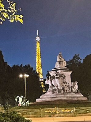 A statue with a pedestal, a tall illuminated structure in the background, and a street lamp. - Bed room in a cosy appartement Eiffel Tower (Paris)