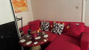 Un canapé rouge avec des coussins à motifs, une petite table ronde sur laquelle est posée une bougie rouge, et un mur orné d’un tableau abstrait rouge.